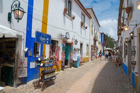 Narrow alley with souvenir shops and colourful clothes, blue and white facades and flowers, R.