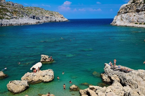 Sunbathing people on rocks on a coast with deep blue water and sunny sky, Anthony Quinn Bay, Vagies
