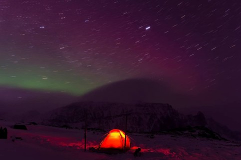 Northern Lights (Aurora borealis) and star trails above an illuminated tent in the valley Stuor