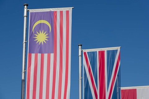 Several flags of different countries fly side by side under a clear blue sky, Malaysian flag,