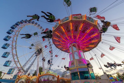 A funfair at dusk with illuminated chain carousel and Ferris wheel, Europa Rad, rides, wave flight,