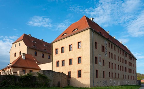 Large, historic building with light-coloured walls and red roof under a blue sky, castle, today