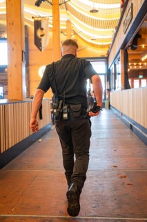 A man in safety equipment walks through an empty, well-lit wooden marquee, Canstatter Wasen,
