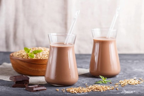 Organic non dairy oats chocolate milk in glass and wooden plate with oats seeds on a black concrete