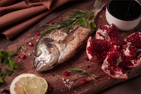 Fried dorado fish, with spices and herbs, on a wooden board, pomegranate sauce, close-up, no people