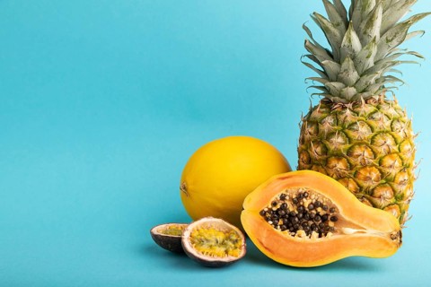 Ripe cut papaya, pineapple, melon, passion fruit, on blue pastel background. Side view, copy space.