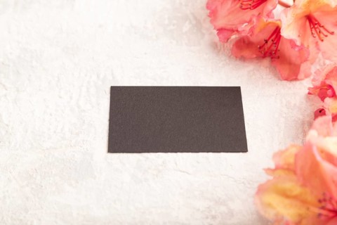 Black business card with pink azalea flowers on gray concrete background. side view, copy space,