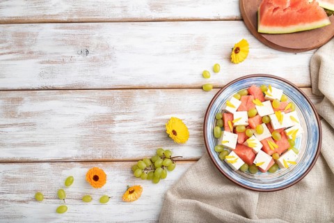 Vegetarian salad with watermelon, feta cheese, and grapes on blue ceramic plate on white wooden