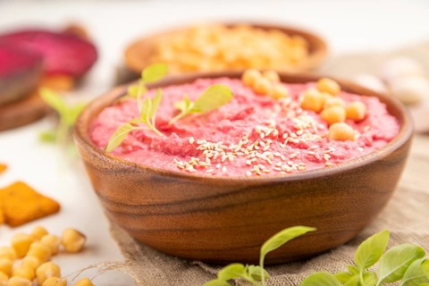 Hummus with beet and microgreen basil sprouts in wooden bowl on a white wooden background and linen