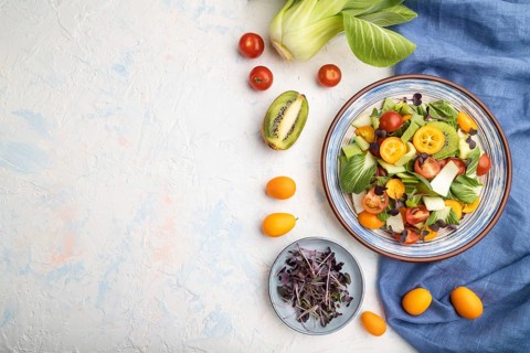 Vegetarian salad of pac choi cabbage, kiwi, tomatoes, kumquat, microgreen sprouts on a white