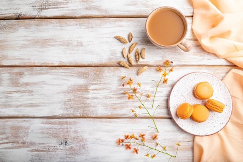 Orange macarons or macaroons cakes with cup of apricot juice on a white wooden background and