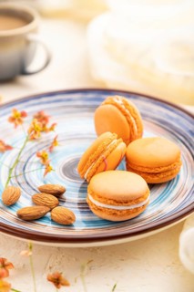 Orange macarons or macaroons cakes with cup of coffee on a white concrete background and linen
