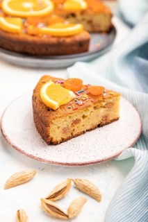 Orange cake with almonds and a cup of coffee on a white concrete background and blue linen textile.