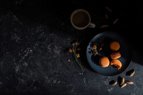 Orange macarons or macaroons cakes with cup of coffee on a black concrete background. Hard light,