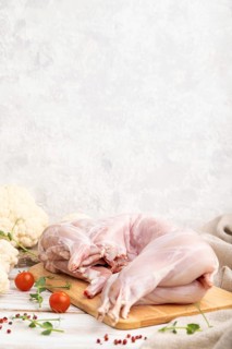 Whole raw rabbit with cauliflower, tomatoes and spices on a white wooden background and linen