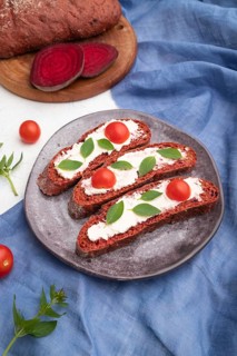 Red beet bread sandwiches with cream cheese and tomatoes on white concrete background and blue