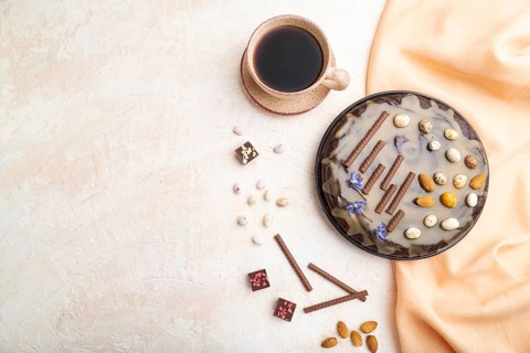 Homemade chocolate brownie cake with caramel cream and almonds with cup of coffee on a white