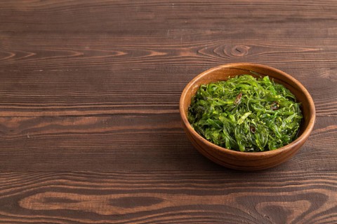 Chuka seaweed salad in wooden bowl on brown wooden background. Side view, copy space