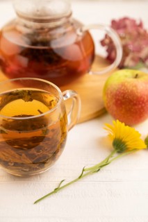 Red tea with herbs in glass teapot on white wooden background. Healthy drink concept. Top view,