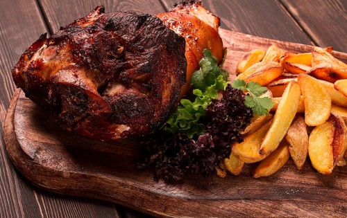 Pork knuckle, in soy-honey sauce, with fried potatoes, on a wooden chopping board, homemade, no