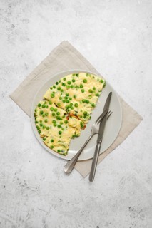 Omelet with fresh green peas and cheese on a plate on a grey stone tabletop