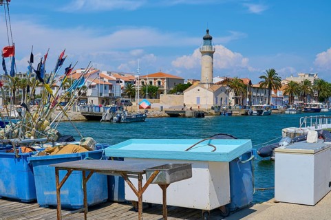 Coastal town with colourful houses and palm trees, boats in the water and a lighthouse, on a sunny