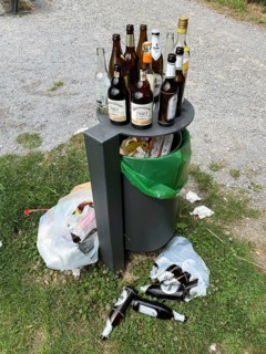 Overflowing rubbish bin, with lots of rubbish, glass bottles next to it, party rubbish, at a