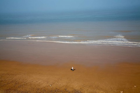 Overhead oblique view of a man walking across wide sandy beach at low tide, Overstrand, Norfolk,