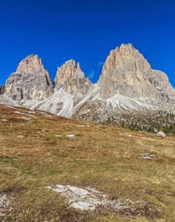 Wide meadow landscape in front of an impressive mountain backdrop on the Sella Pass under a clear