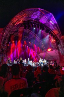 Large concert on an illuminated stage with orchestra, surrounded by an impressed audience,