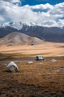 Off-road vehicle on a gravel track, glaciated and snow-covered peaks, Ak Shyrak Mountains, near