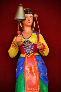 Wooden figure, colourfully painted, woman in traditional traditional costume strikes bell, bell