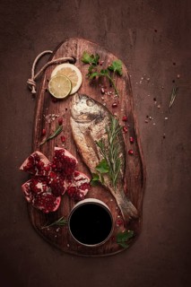 Fried dorado fish, with spices and herbs, on a wooden board, pomegranate sauce, close-up, no people