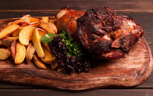 Pork knuckle, in soy-honey sauce, with fried potatoes, on a wooden chopping board, homemade, no
