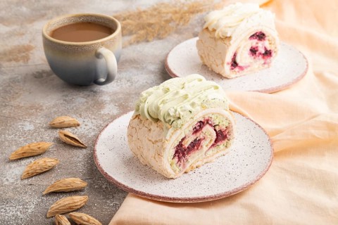 Roll biscuit cake with cream cheese and jam, cup of coffee on brown concrete background and orange