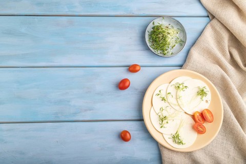 White cheese with tomatoes and cilantro microgreen on blue wooden background and linen textile. top