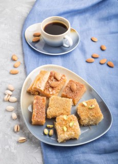 Traditional arabic sweets (basbus, kunafa, baklava) and a cup of coffee on a gray concrete