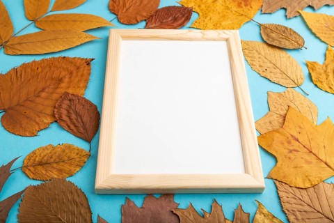 Composition with yellow and brown autumn leaves and wooden frame mockup on blue pastel background.