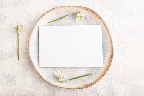 White paper invitation card, mockup with galanthus snowdrop flowers on ceramic plate and gray
