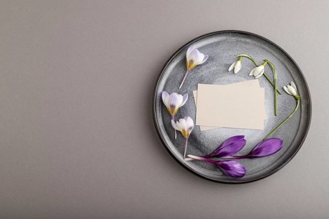 Gray paper invitation card, mockup with crocus and galanthus flowers on ceramic plate and gray