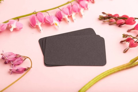 Black business card with pink dicentra, broken heart flowers on pink pastel background. side view,