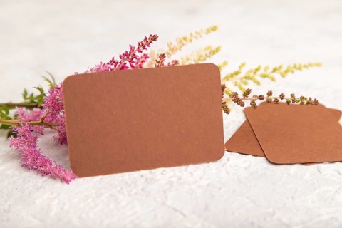 Brown paper business card mockup with purple astilbe flowers on gray concrete background. Blank,