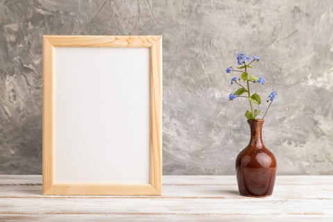 Wooden frame with blue forget-me-not flowers in ceramic vase on gray concrete background. side