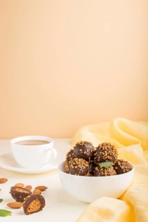 Chocolate caramel ball candies with almonds and a cup of coffee on a white and orange background