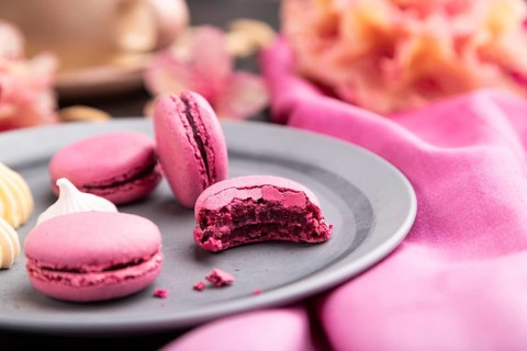 Purple macarons or macaroons cakes with cup of coffee on a black concrete background and pink