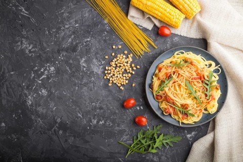 Corn noodles with tomato sauce and arugula on a black concrete background and linen textile. Top