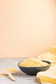 Blue ceramic bowl with raw golden rice and wooden spoon on a gray and orange background and yellow