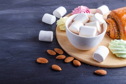 A cup of hot chocolate with marshmallow, bun and meringues on black wooden background. close up,