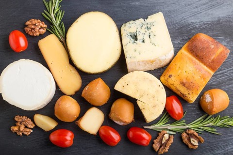 Set of different types of cheese with rosemary and tomatoes on a black wooden background. Top view,