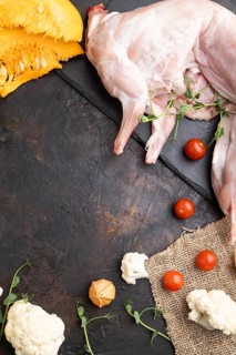 Whole raw rabbit with pumpkin, tomatoes, pea sprouts on a black concrete background and linen